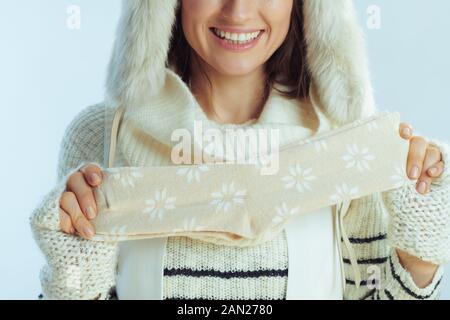 In der Nähe der lächelnden eleganten 40 Jahre alten Frau in weiß gestreiften Pullover, Schal und Ohrenklappenhut, die zwei Wintersocken auf dem hellblauen Winterrücken zeigt Stockfoto