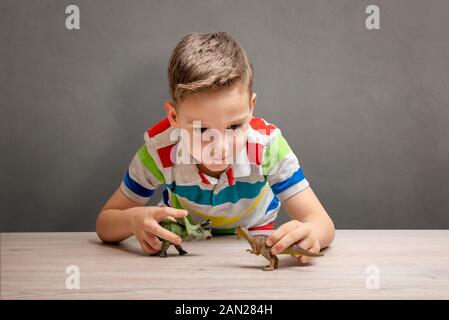 Junge spielt mit Dinosauriern auf dem Schreibtisch. Konzept der Dinosaurier Obsession. Saubere Wände im Hintergrund Stockfoto