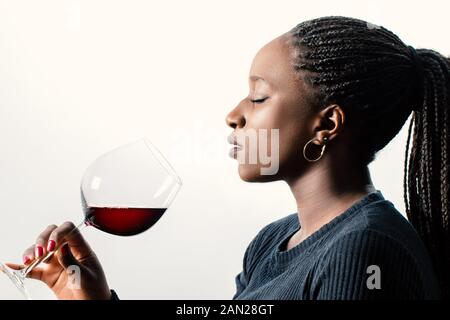 Close up Seitenansicht Portrait von afrikanischen Frauen Wine Enthusiast riechen Rotwein Aroma. Frau mit geflochtenem Haar und Augen geschlossen gegen Weiße isoliert Stockfoto