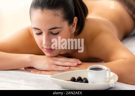 Close up Portrait von entspannt Frau Festlegung auf der Couch mit den Augen in Spa geschlossen. Hot Chocolate Massage Öl in der Schüssel neben Mädchen. Stockfoto