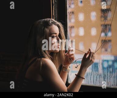 Schöne blonde Frau mit langem Haar an der Regentropfen auf dem Fenster suchen Stockfoto
