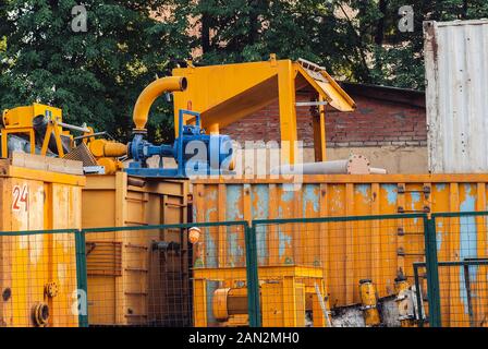 Leistungsstarke Elektromotoren in Blau für die moderne industrielle Ausrüstung und gelbe Behälter hinter dem Grün stahl Zaun bemalt. Stockfoto