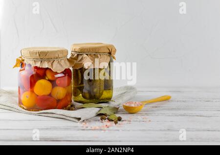 Zwei Glas Gläser vergorene Gurken, Tomaten. Gemüse auf einem hellen Hintergrund. Über textile Hellgrau. Gärung ist eine Quelle von Probiotika. cop Stockfoto