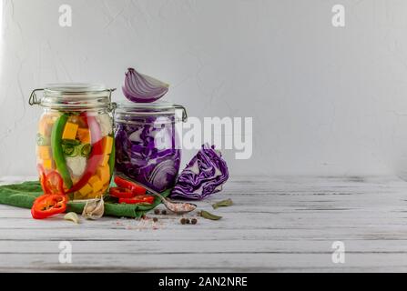 Zwei Gläser von fermentierten Rotkohl, Chili, Paprika, Blumenkohl, Zwiebeln, pumkin, Gemüse auf einem hellen Hintergrund. Über textile Grün. Fermentation Stockfoto