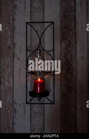 Eine brennende rote Kerze auf eine Holzwand. Stockfoto