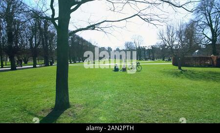 Leute sitzen auf Gras und entspannen im grünen Stadtpark am sonnigen Tag, Wochenende Stockfoto
