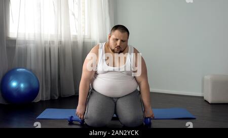 Erschöpft Fat Man sitzt auf dem Boden mit Hanteln, anstrengenden Training Programm, Sport Stockfoto