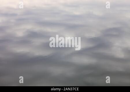 Abstrakter Hintergrund - Reflexion des trüben, neutralen Himmels in den Mustern der Wasseroberfläche mit dunklen und glänzenden Flecken Stockfoto