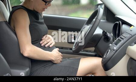 Schwangere Frau in offiziellen Kleidung im Auto sitzen und Leiden von Bauch schmerzen Stockfoto