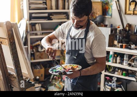 Männliche Maler bei art studio Zuhause im Prozess des Malens nachdenklich Stockfoto