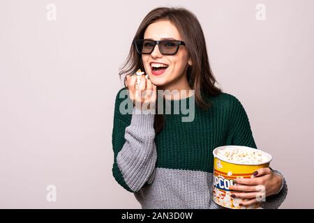 Porträt von einem aufgeregten Mädchen in der 3D-Brille holding Eimer Popcorn und entfernten Blick auf gelben Hintergrund isoliert Stockfoto