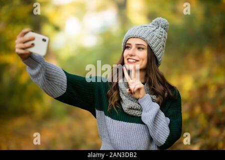 Positive Frau, die selfie während Kaffee trinken im Herbst Park. Stockfoto