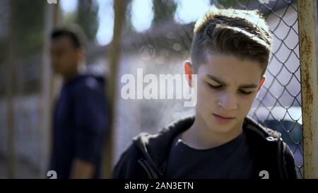 Verärgert jugendlich Jungen lehnte sich auf Metall Zaun, mit der Gesellschaft aufgegeben, Waisenhaus Stockfoto