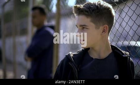 Nachdenklich jugendlich Jungen lehnte sich auf Metall Zaun, mit zukünftigen umgekippt, Waisenhaus Stockfoto