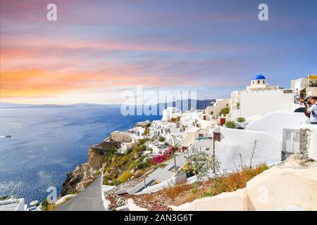 Touristen genießen und ein farbenfroher Sonnenuntergang und Meerblick Foto aus der weißen Stadt Oia auf der griechischen Insel Santorini. Stockfoto