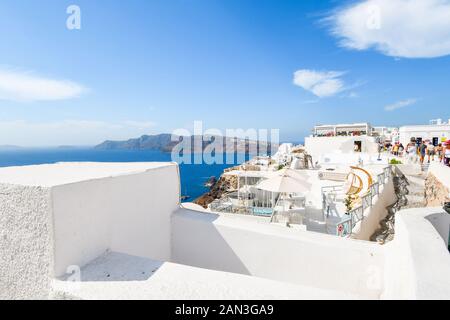 Touristen genießen den oberen Gehweg in Oia, Griechenland, auf einem langen Sommertag mit Blick auf das Ägäische Meer auf der Insel Santorini. Stockfoto