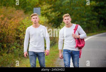 Billige Reisen. Freundschaft Konzept. Männer Trampen. Mann lässigen Stil reisen mit Rucksack Reisenden per Anhalter fahren auf der Autobahn. Auf dem Weg nach Hause. Zukunft. Zwillinge entlang der Straße laufen. Zwei Brüder Abenteuer gehen. Stockfoto