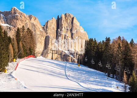 Leere Piste mit einem Sessellift im Hintergrund am Fuße des felsigen Gipfeln der Dolomiten an einem klaren Wintertag Stockfoto