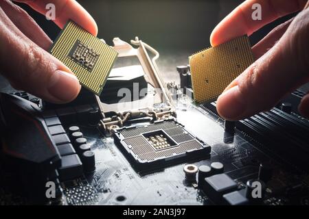 Hände zeigen verschiedenen Prozessoren. Zwei CPUs vor dem Hintergrund der Hauptplatine. Die Auswahl des Prozessors, der Vorteil der Marke und Stockfoto