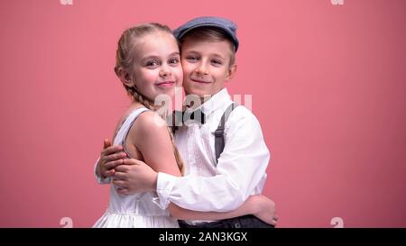 Happy Kids Paar umarmen und uns auf die Kamera, auf rosa Hintergrund isoliert Stockfoto