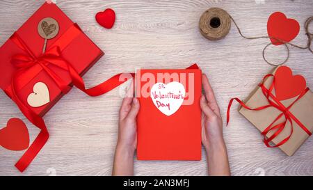 Frau mit Grußkarte mit St Valentines Tag Phrase, Geschenkboxen auf Tisch Stockfoto