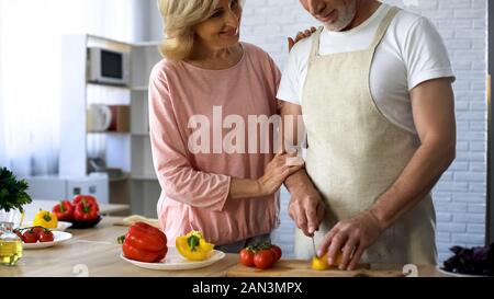 Ältere Mann schneiden frischen Pfeffer in der Küche, Frau umarmt Liebe, Nähe Stockfoto