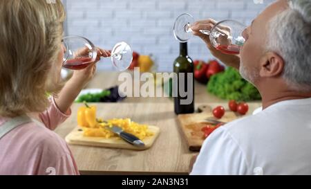 Älterer Mann und Frau trinken Rotwein Zuhause, Kochen Salat zum Abendessen, Datum Stockfoto