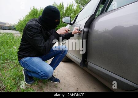 Bricht in den Wagen. Theft Auto. Der übeltäter in eine schwarze Maske öffnet eine Tür in einem Auto. Stockfoto