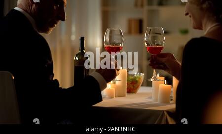 Pensionierte elegantes Paar toasten Holding Weingläser, romantisches Abendessen Kerzen Stockfoto