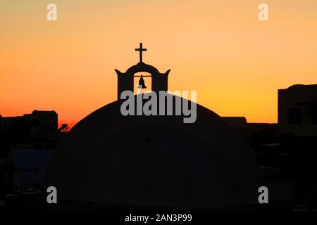 Eine Kirchenkuppel mit Glocke und Ordenskreuz in der Stadt Oia in Santorini, Griechenland. Stockfoto