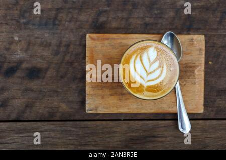 Draufsicht eine Tasse Cappuccino oder Latte mit Blumenmuster aus Latte Art in transparentem Glas auf Holztablett und Tisch. Stockfoto