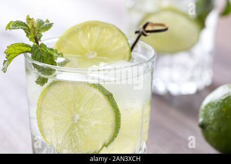 Eine Nahaufnahme von einem eisigen Glas Wasser mit Kohlensäure mit Kalk und mit Minze garniert. Stockfoto