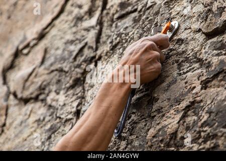 Eine Nahaufnahme von Advanced Klettern Ausrüstung im Einsatz als die Hand eines Mannes greift auf ein gesichertes Gerät belay, Gesundheit und Sicherheit während der riskanten Sport Stockfoto