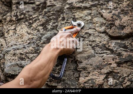 Eine Nahaufnahme auf die muskulösen Arm von einem kaukasischen Männlich, Festsetzung eines belay Seil Ankerpunkt in einem robusten limestone Crag während Klettern Abenteuer Stockfoto