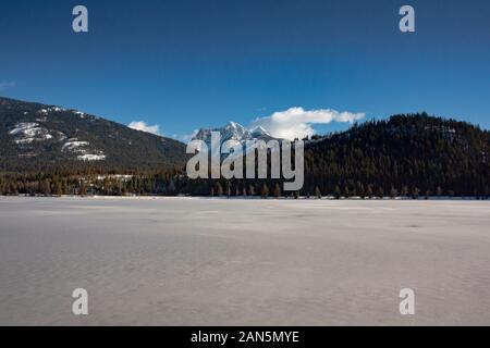 Auf der Suche über einen gefrorenen See winter Stier, in Richtung der fernen, schneebedeckten Ibex Peak, im Kabinett Berge, Lincoln County im US-Bundesstaat Montana. Stier See ist Stockfoto