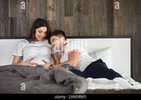 Ein junges Ehepaar, das auf ein Baby wartet. Ein wunderschönes Paar, das im Schlafzimmer liegt, plant die Geburt eines Babys. Erstes Kind, Postpartum, junge Familie Stockfoto