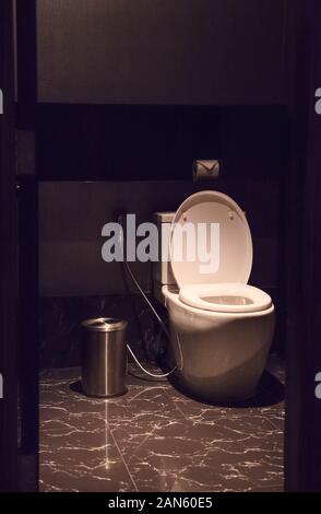 Selektive konzentrierte sich auf weißer Keramik spülen wc Schüssel Mischbatterie mit Toilettenpapier, Bidet spray Dusche und Papierkorb in Luxus Fliesenboden Badezimmer zurück Stockfoto