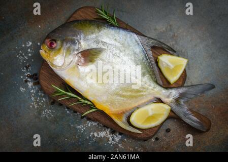 Frische butterfische Fisch mit Kräuter Gewürze Rosmarin und Zitrone auf Holz Schneidebrett und schwarze Platte Hintergrund/Raw schwarz butterfische Fisch Stockfoto