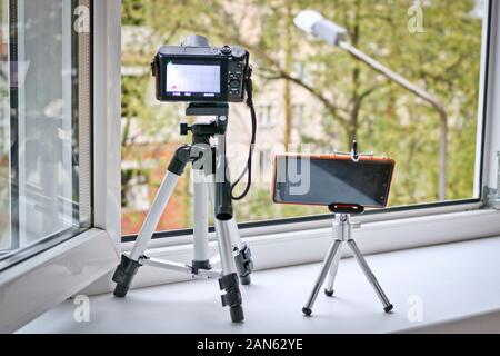 Kamera und Smartphone auf Stative vor einem offenen Fenster. Zeitraffer Fotografie - Smartphone vs Kamera. Stockfoto