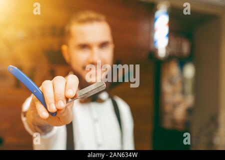 Die Jungen gut aussehenden bärtigen Friseur mit einem Rasiermesser in der Hand. Friseur Stockfoto