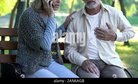 Rentner leiden Herzinfarkt im Park, Frau ruft den Notdienst Stockfoto