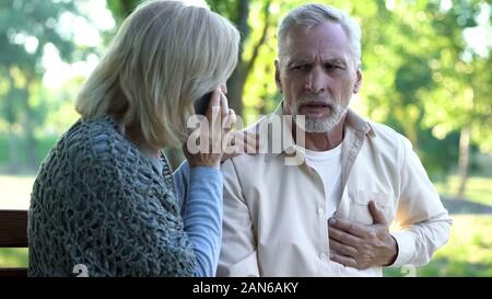 Alte Paar sitzt auf der Bank, der Mensch leiden Arrhythmie, Frau ruft Not Stockfoto