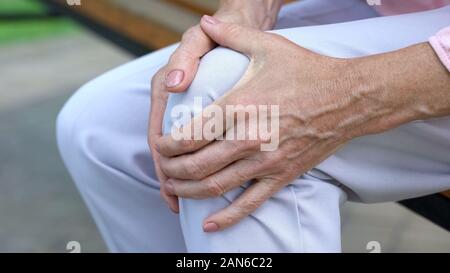 Alte Dame Knie berühren, sitzt auf der Bank, Schmerzen in den Gelenken, Probleme mit Knie Stockfoto