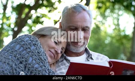 Liebevolle reife Familie beobachten, Photoalbum, in Erinnerung an die Kindheit ihrer Kinder Stockfoto