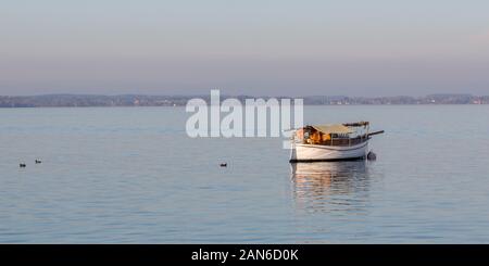 segelboot mit gefaltetem Mast am Chiemsee (größter bayerischer See) verankern. Schwache Reflexion auf dem Wasser. Am späten Nachmittag Licht, Beginn des Morgengrauen. Stockfoto