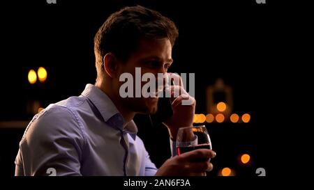 Schön lächelnden jungen Mann am Telefon sprechen und trinken Rotwein, Entspannung Stockfoto