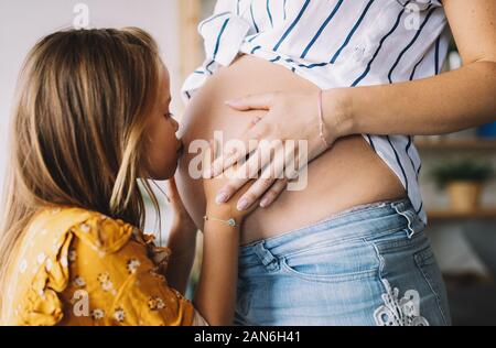 Glückliches Kind Mädchen umarmt Bauch der schwangeren Mutter Stockfoto