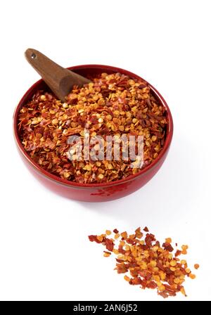 Vertikal, chiliflocken in einem roten Schüssel mit kleinen Holzlöffel auf weißem Hintergrund Stockfoto