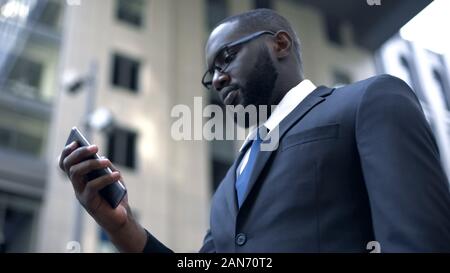 Ernsthafte afro-amerikanischen Geschäftsmanns, der auf dem Smartphone, Business Application Stockfoto