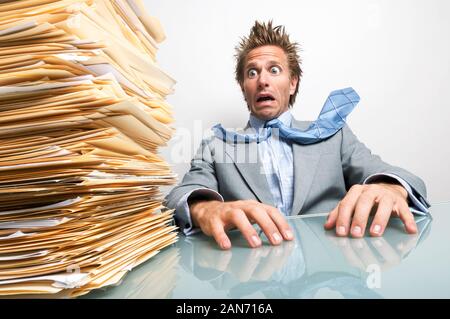 Betonte Geschäftsmann an seinem Schreibtisch zu einem großen Stapel der unerledigten Papierkram suchen Sitzen Stockfoto